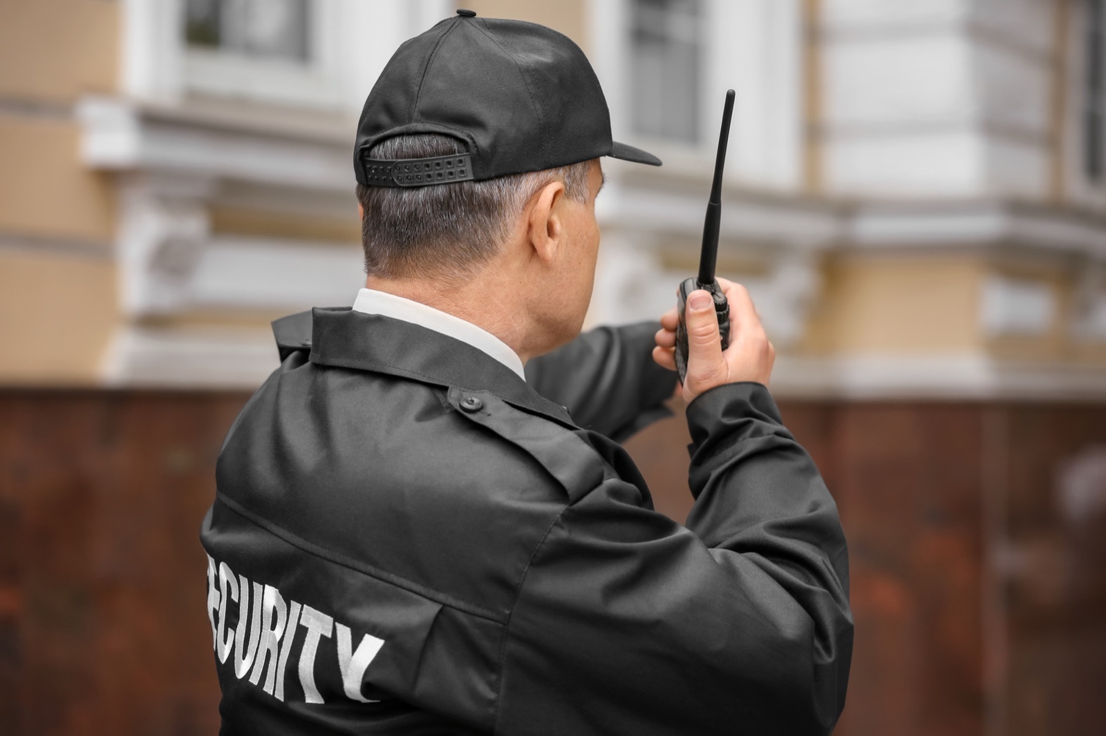 Sicherheitskraft in dunkler Dienstjacke spricht vor einem Gebäude in ein Funkgerät